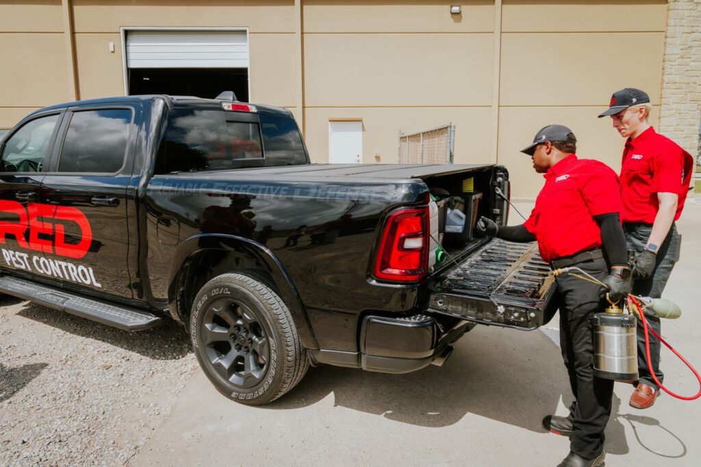 Red Pest Control technician next to branded service vehicle